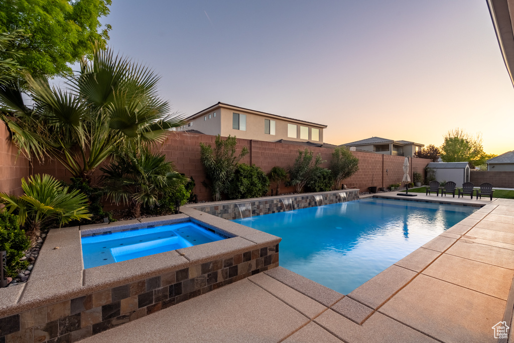 Pool at dusk with a patio area, pool water feature, and an in ground hot tub