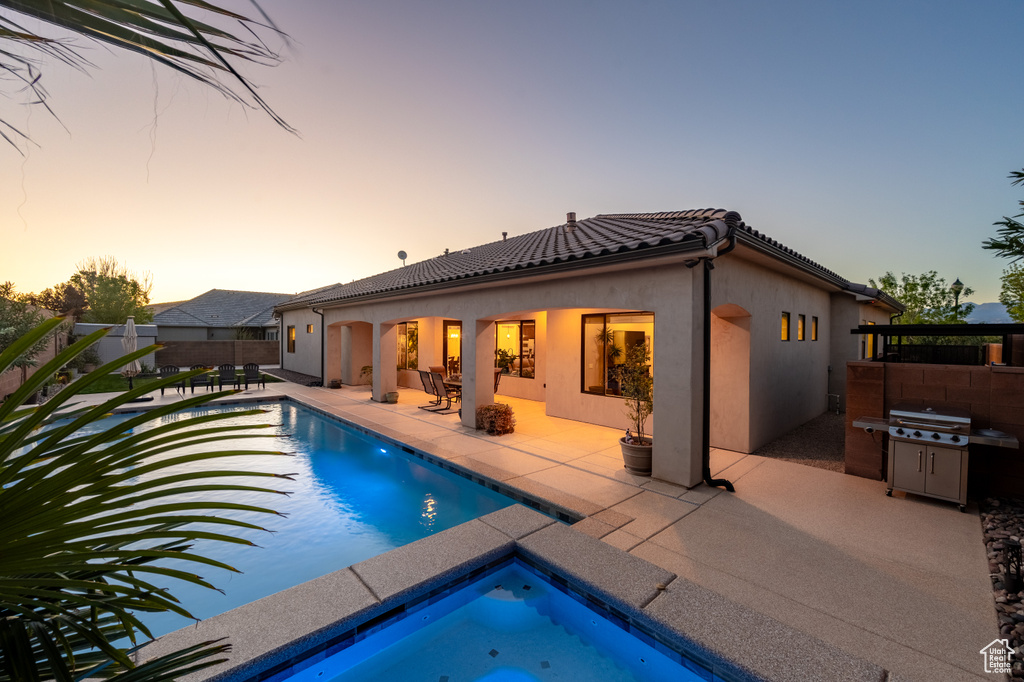 Pool at dusk featuring a patio area and an outdoor hot tub