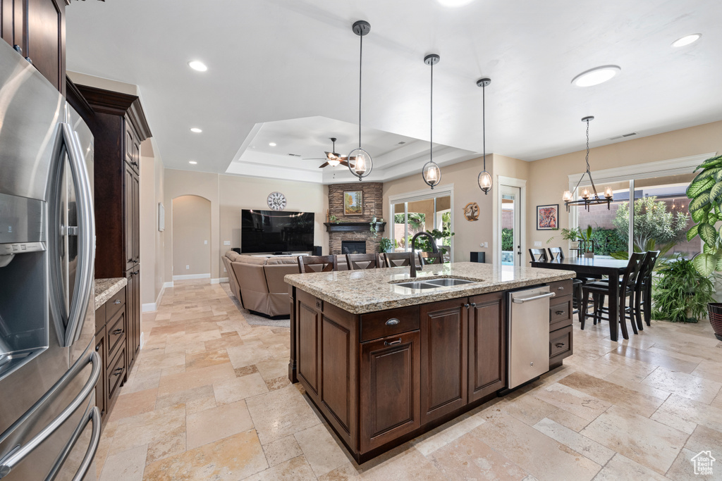 Kitchen featuring a fireplace, ceiling fan with notable chandelier, appliances with stainless steel finishes, sink, and a raised ceiling