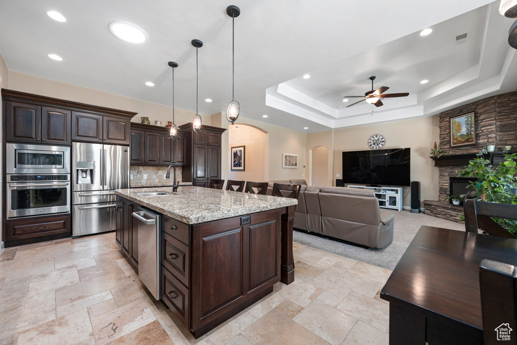 Kitchen with appliances with stainless steel finishes, a stone fireplace, backsplash, a raised ceiling, and light stone countertops