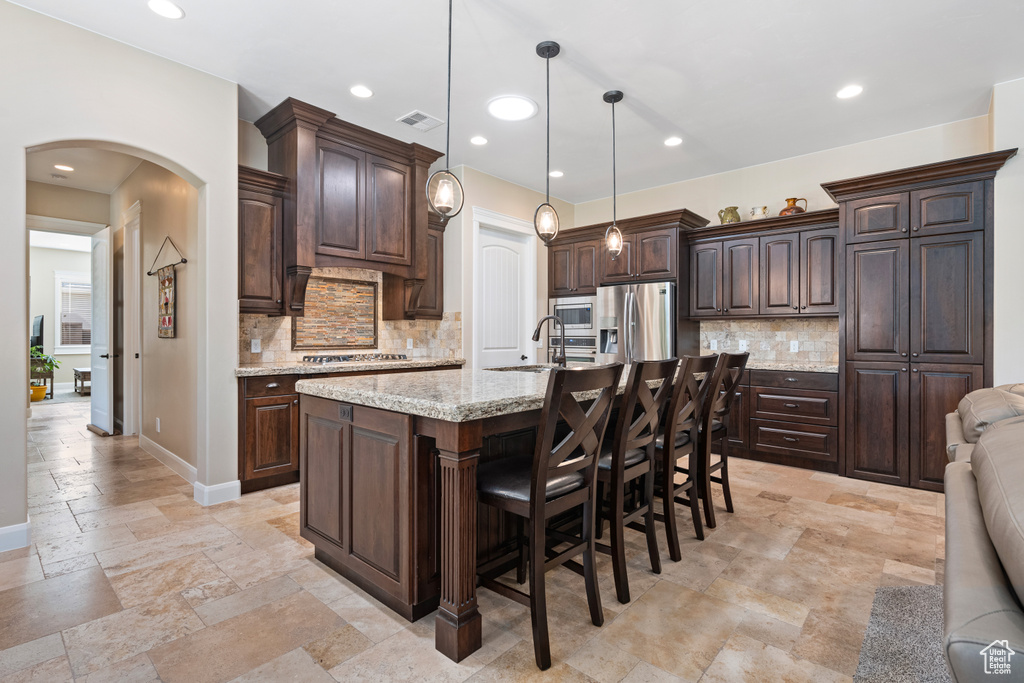 Kitchen featuring tasteful backsplash, dark brown cabinets, stainless steel appliances, and light stone countertops