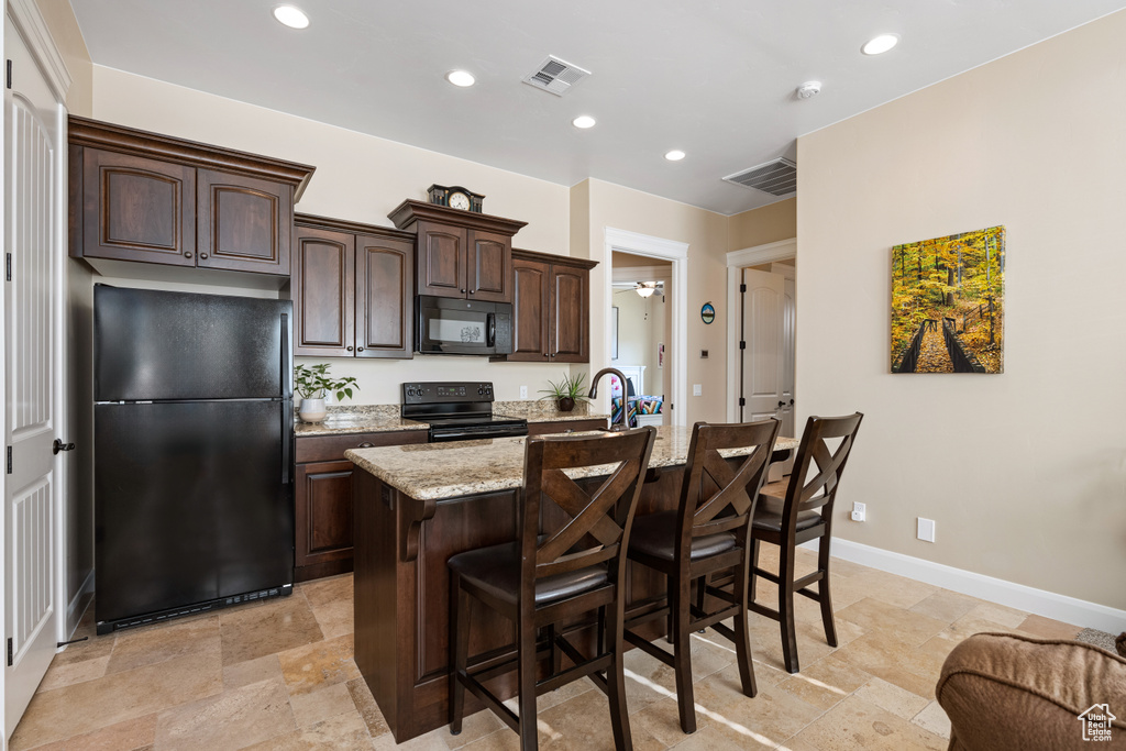 Kitchen with light stone counters, a breakfast bar area, a center island with sink, and black appliances
