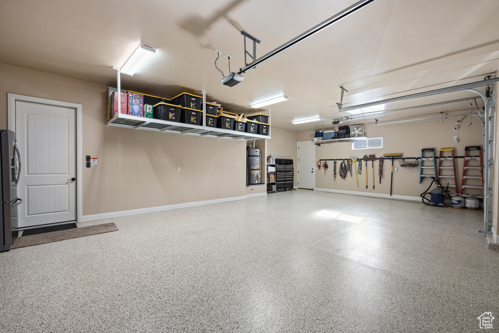 Garage with secured water heater, stainless steel refrigerator with ice dispenser, and a garage door opener
