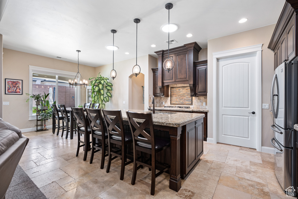 Kitchen featuring light stone counters, a breakfast bar, stainless steel refrigerator, light tile flooring, and pendant lighting