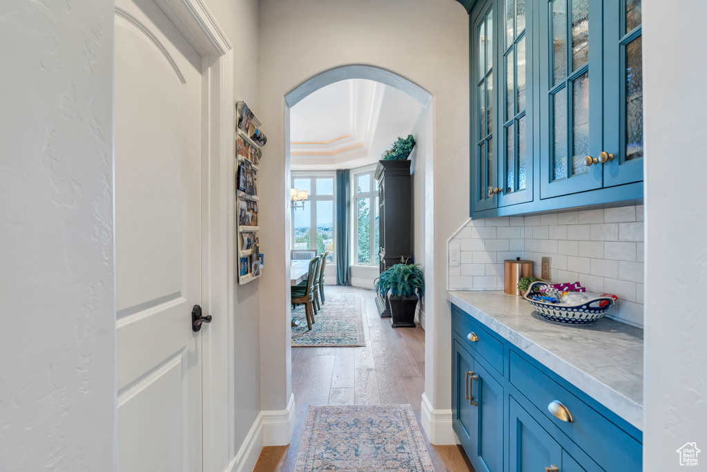 Interior space with blue cabinetry, backsplash, light hardwood / wood-style floors, light stone counters, and ornamental molding