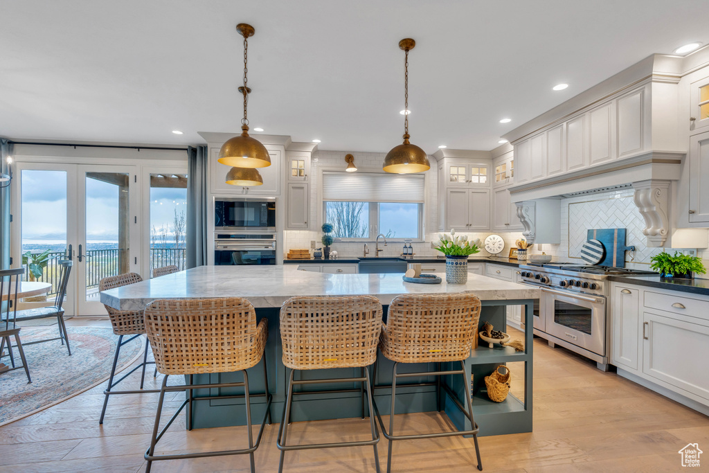 Kitchen with hanging light fixtures, stainless steel appliances, tasteful backsplash, a center island, and light wood-type flooring