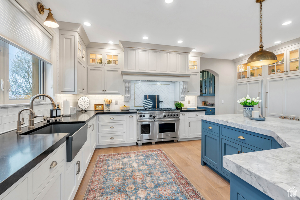 Kitchen with blue cabinets, backsplash, range with two ovens, light hardwood / wood-style flooring, and pendant lighting