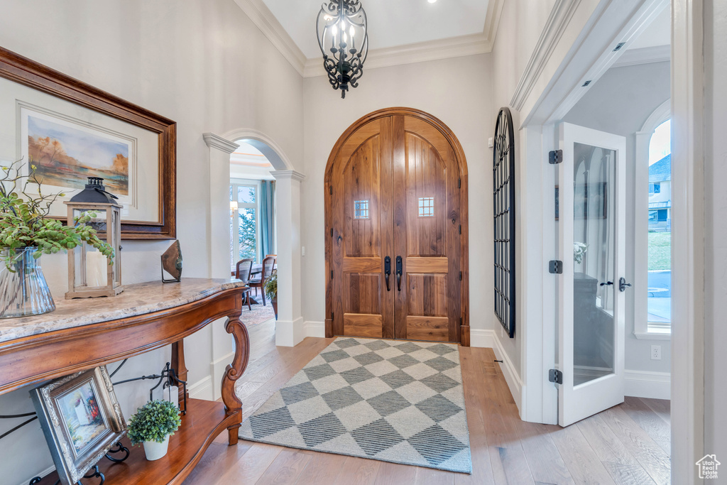 Foyer entrance featuring ornamental molding, ornate columns, light wood-type flooring, and a wealth of natural light