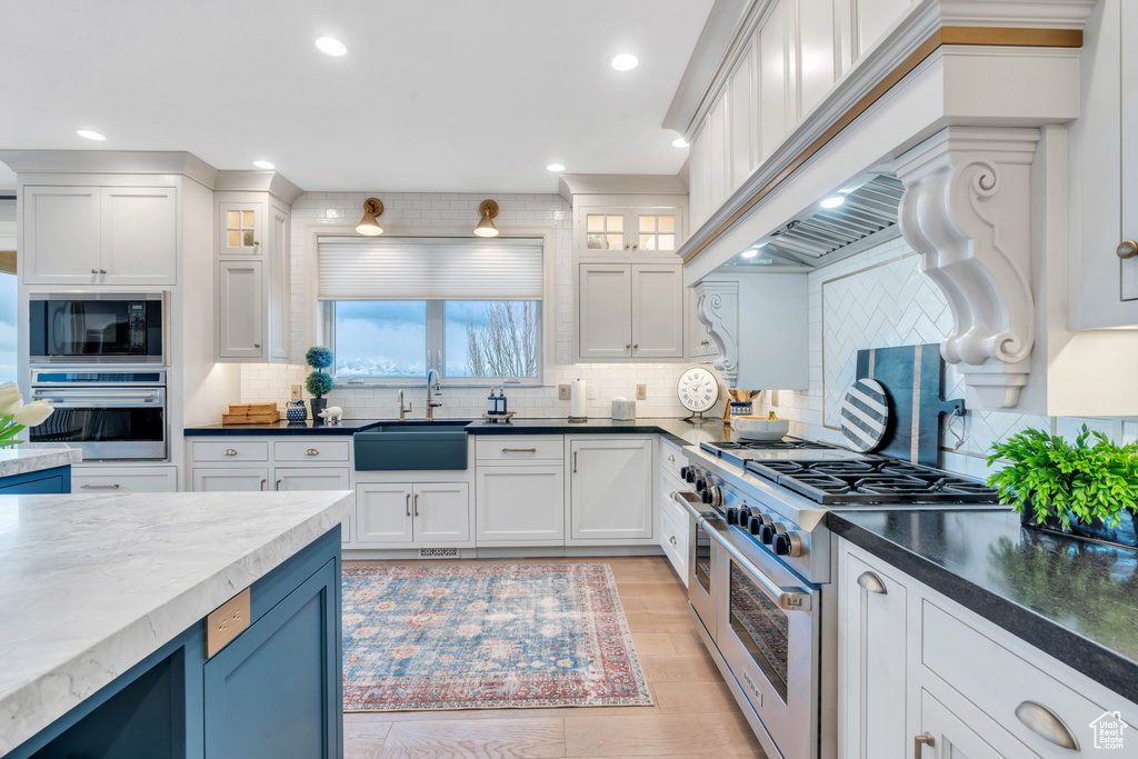 Kitchen with appliances with stainless steel finishes, white cabinets, sink, tasteful backsplash, and blue cabinetry
