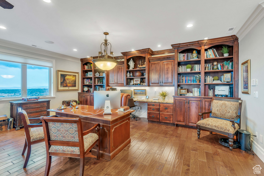 Home office with crown molding, built in desk, and light wood-type flooring