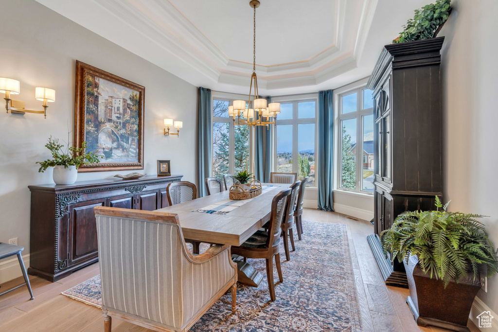Dining area featuring light hardwood / wood-style flooring, crown molding, a raised ceiling, and an inviting chandelier