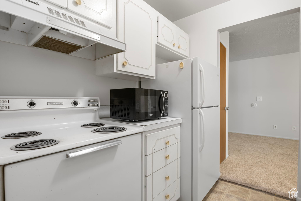 Kitchen with white cabinets, light colored carpet, and white appliances