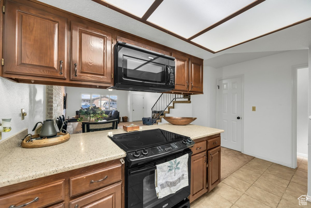 Kitchen featuring black appliances, light tile floors, and light stone counters