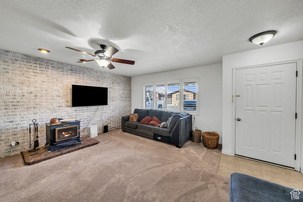 Living room with ceiling fan, brick wall, a textured ceiling, light carpet, and a wood stove