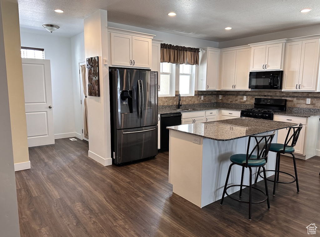 Kitchen with a center island, white cabinetry, dark hardwood / wood-style floors, black appliances, and a breakfast bar area