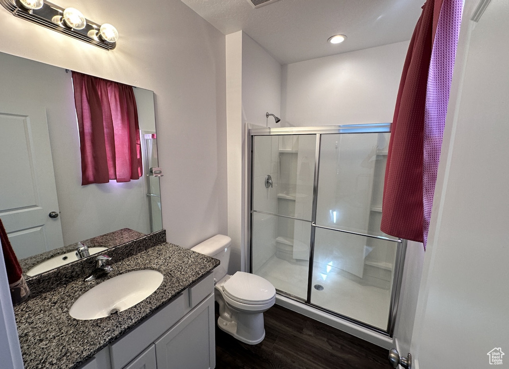 Bathroom featuring wood-type flooring, an enclosed shower, vanity with extensive cabinet space, and toilet