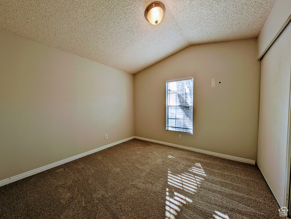 Carpeted spare room with a textured ceiling and lofted ceiling