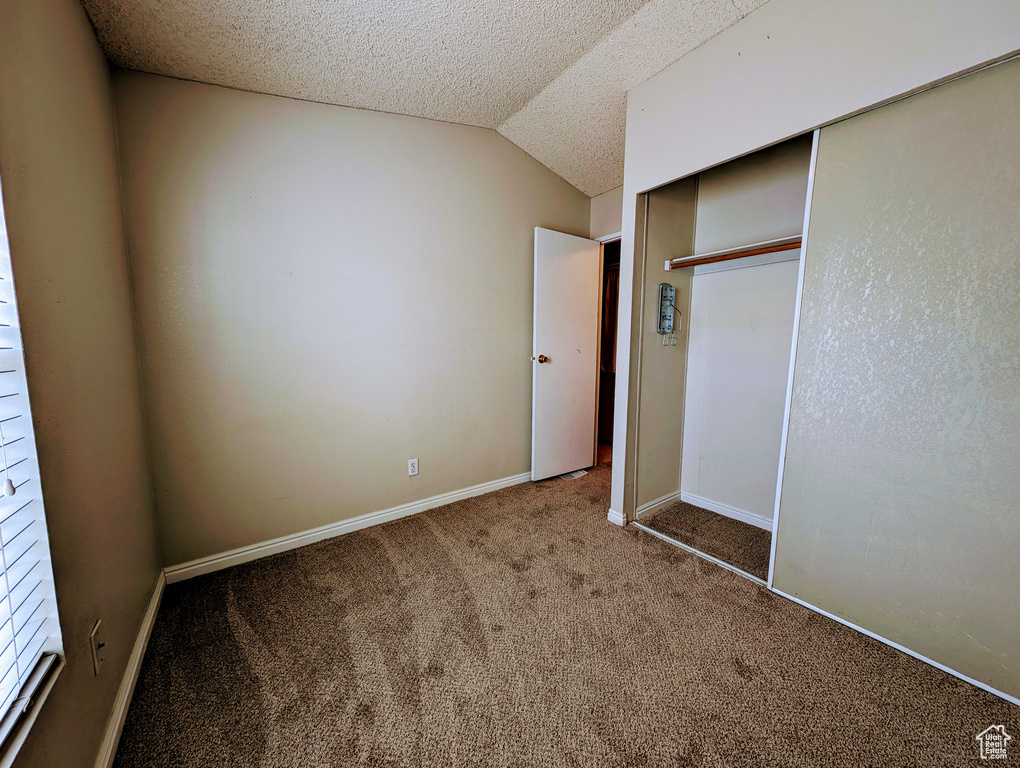 Unfurnished bedroom featuring a textured ceiling, lofted ceiling, a closet, and dark colored carpet