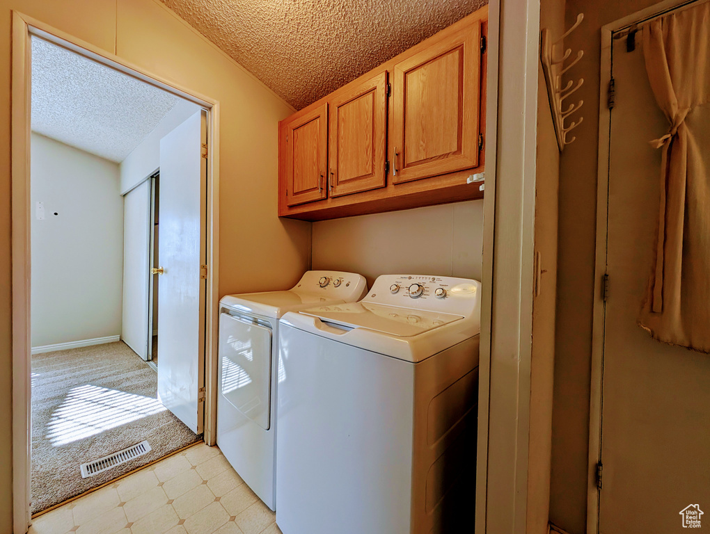 Washroom with a textured ceiling, washing machine and clothes dryer, cabinets, and light tile floors