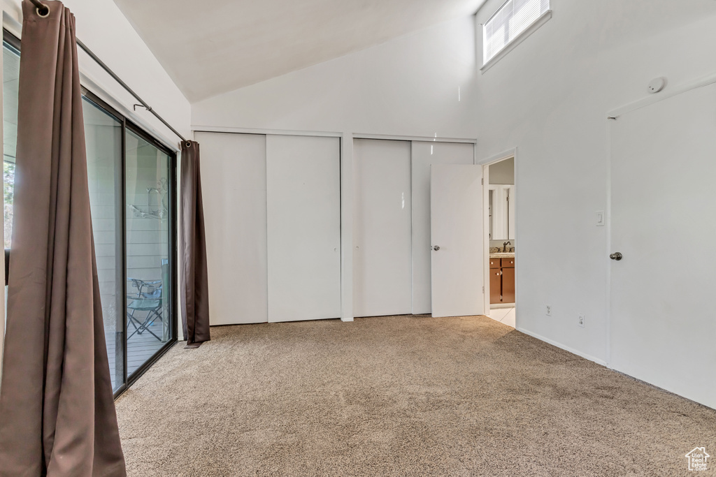 Unfurnished bedroom featuring light colored carpet, high vaulted ceiling, access to exterior, and multiple closets