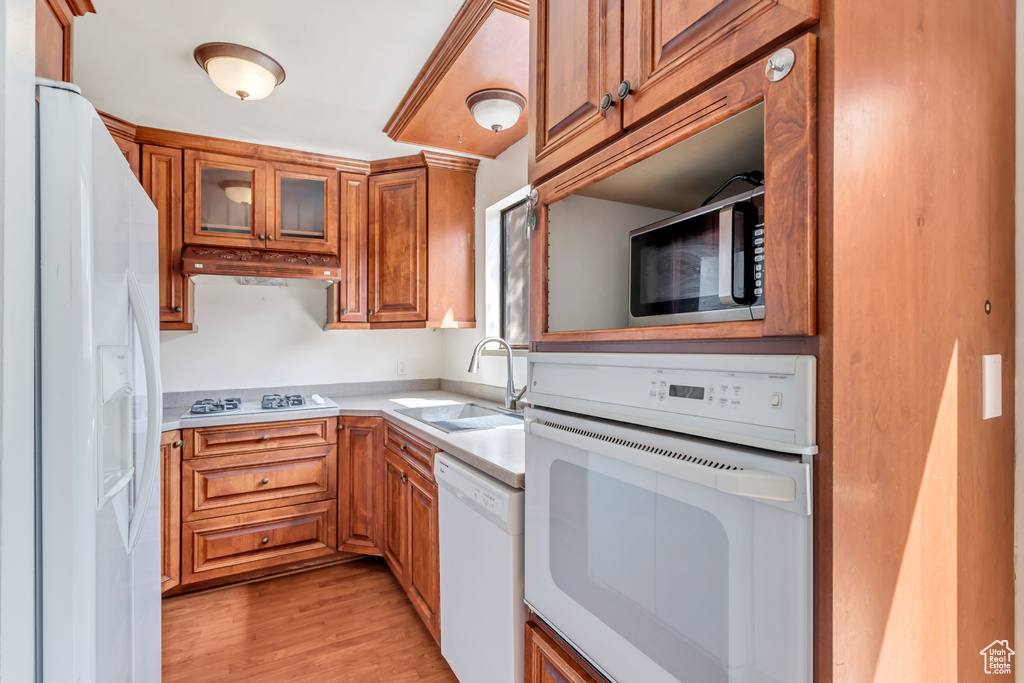 Kitchen with sink, white appliances, light wood-type flooring, and custom range hood