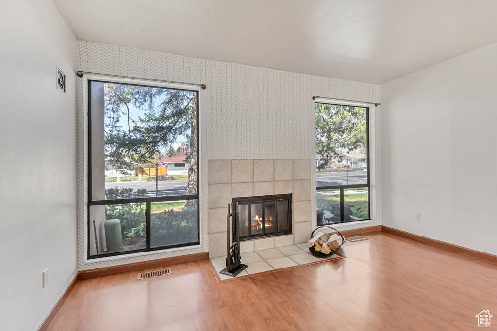 Unfurnished living room with light hardwood / wood-style floors, a healthy amount of sunlight, and a tiled fireplace
