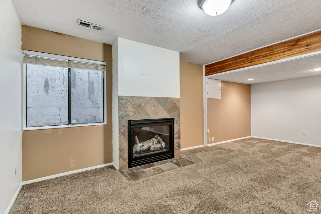 Unfurnished living room with light carpet, a textured ceiling, and a tiled fireplace