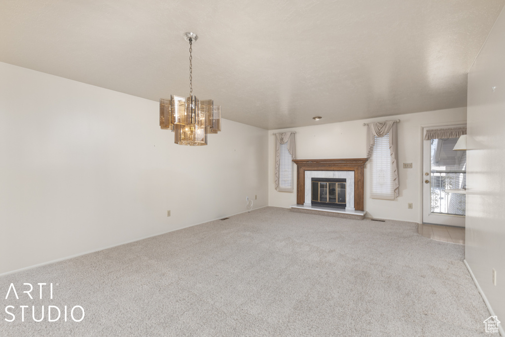 Unfurnished living room featuring an inviting chandelier and light colored carpet