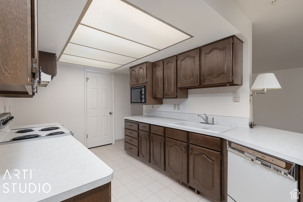 Kitchen featuring dark brown cabinetry, sink, white appliances, and light tile flooring