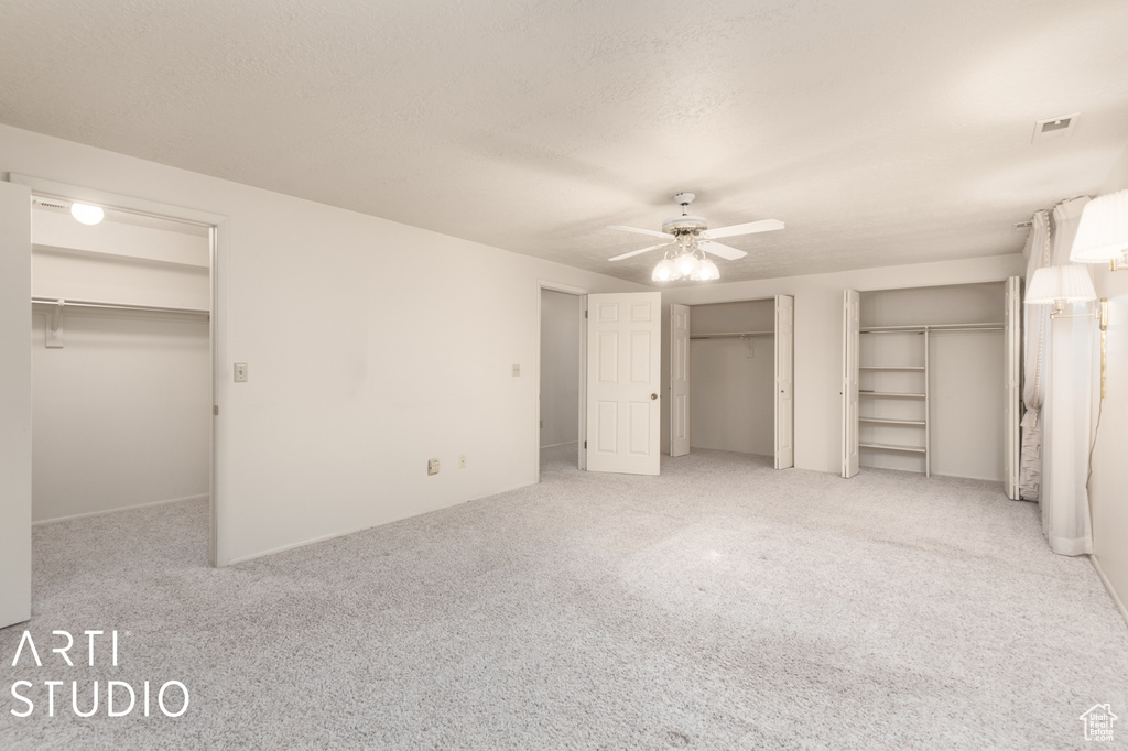 Unfurnished bedroom with two closets, ceiling fan, and light carpet