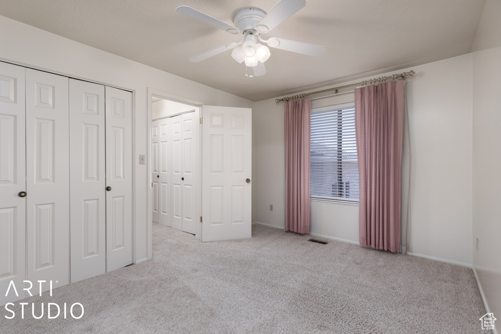 Unfurnished bedroom featuring light colored carpet, ceiling fan, and two closets