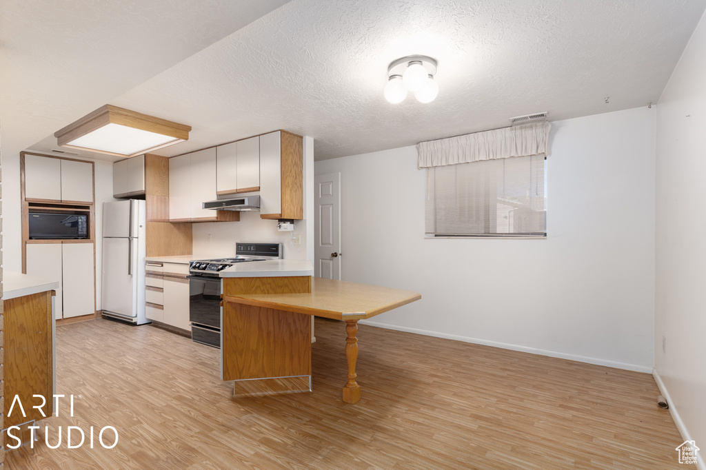 Kitchen with white fridge, white cabinets, light hardwood / wood-style floors, black microwave, and stove