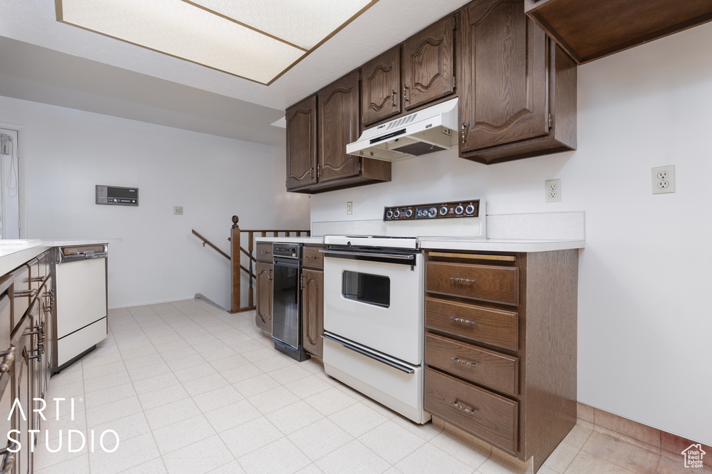 Kitchen with dark brown cabinetry, white appliances, and light tile floors