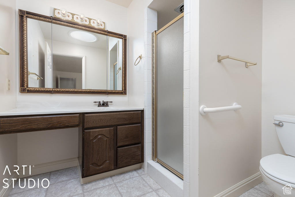 Bathroom featuring a shower with door, toilet, tile floors, and vanity