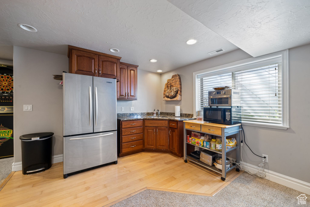 Kitchen with stainless steel refrigerator, a healthy amount of sunlight, light hardwood / wood-style flooring, and stone countertops