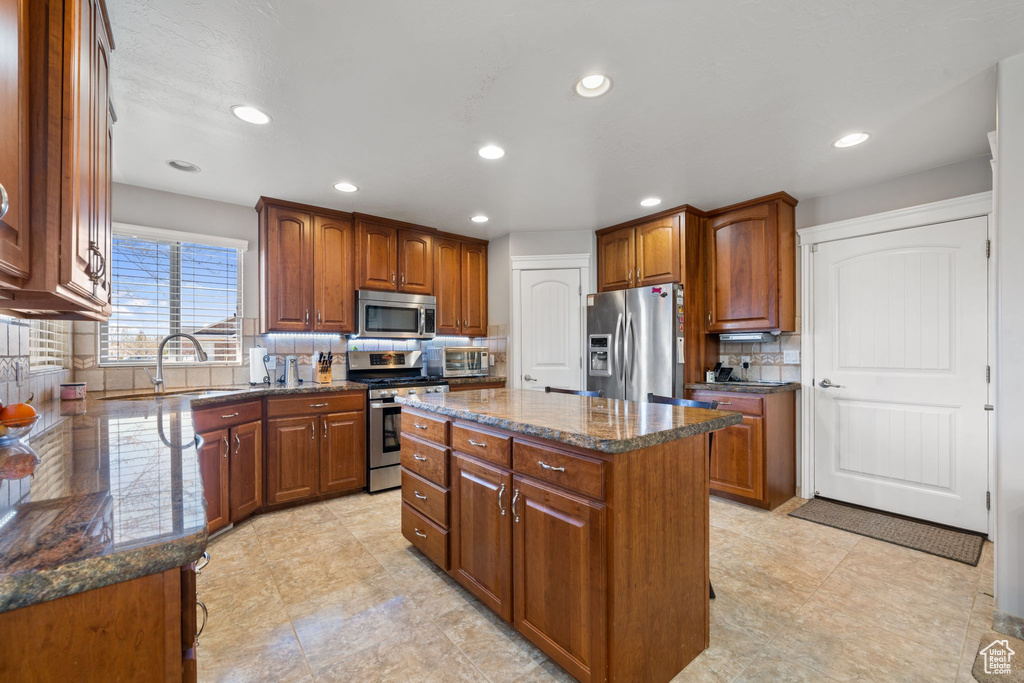 Kitchen featuring backsplash, stainless steel appliances, sink, a kitchen island, and dark stone countertops