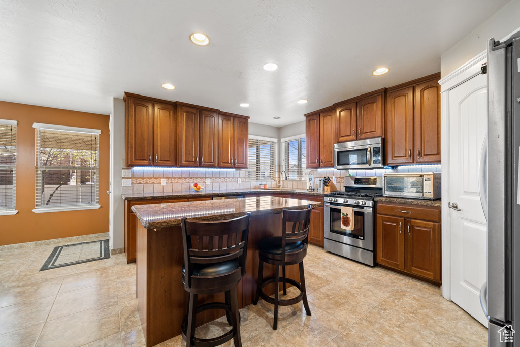 Kitchen featuring appliances with stainless steel finishes, a kitchen island, light tile flooring, backsplash, and a kitchen breakfast bar