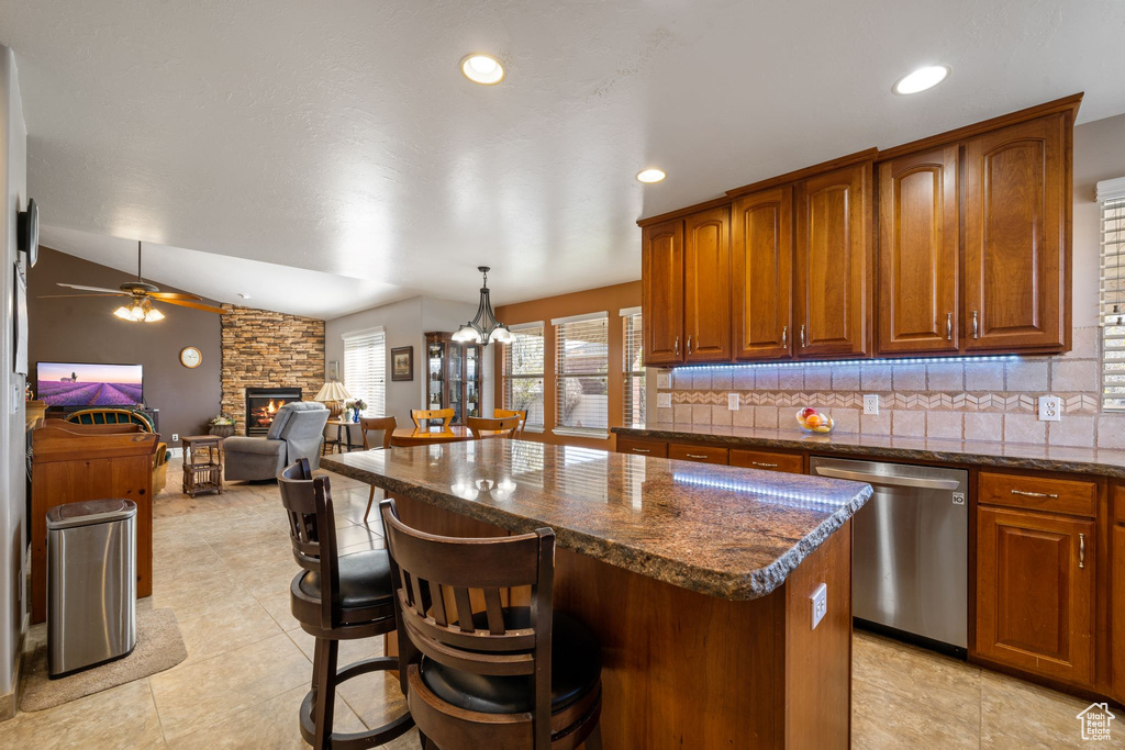Kitchen featuring a center island, a fireplace, backsplash, stainless steel dishwasher, and lofted ceiling