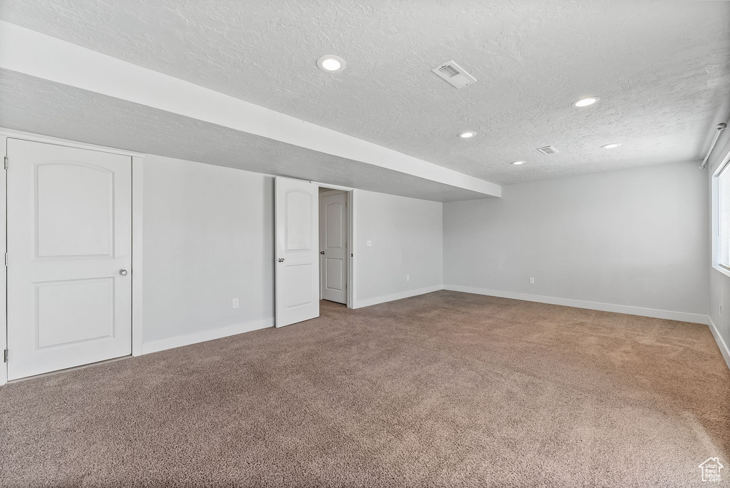Basement featuring a textured ceiling and light carpet