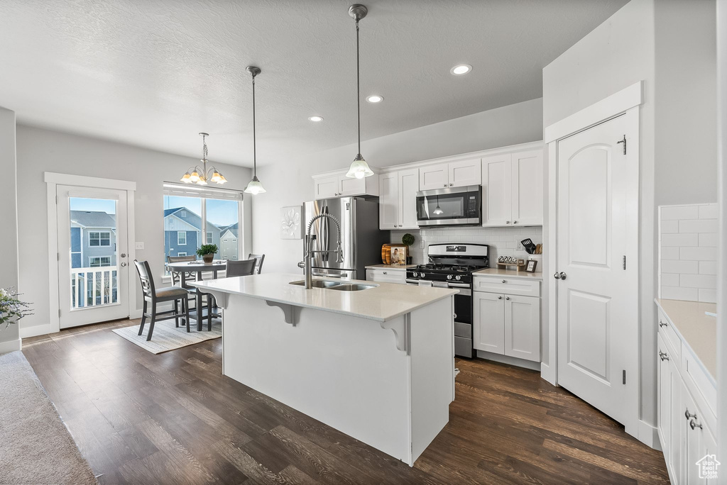 Kitchen with appliances with stainless steel finishes, dark wood-type flooring, white cabinetry, and hanging light fixtures