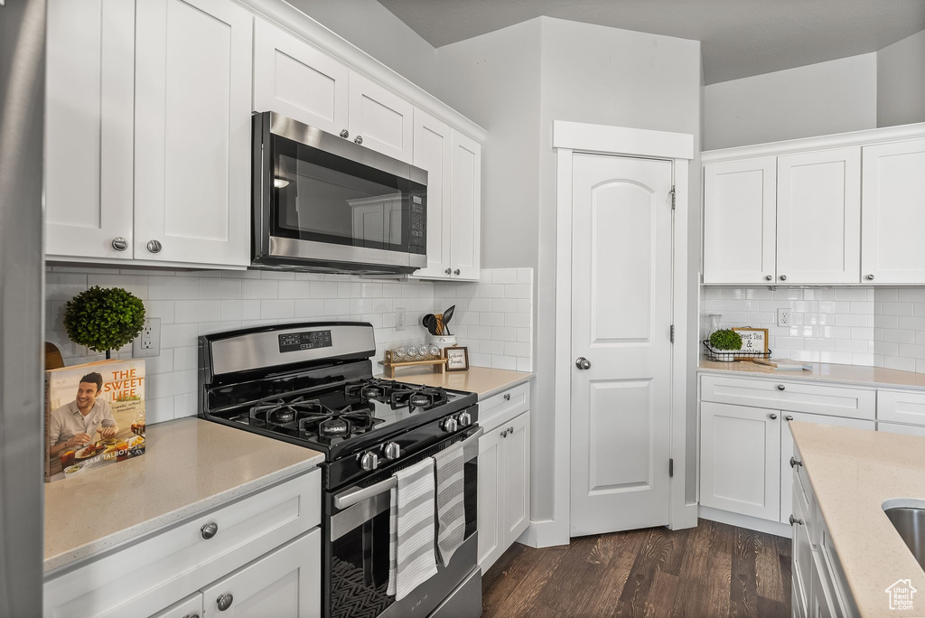Kitchen featuring white cabinets, tasteful backsplash, stainless steel appliances, and dark hardwood / wood-style floors
