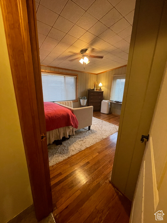 Bedroom with ceiling fan, light hardwood / wood-style floors, and wooden walls