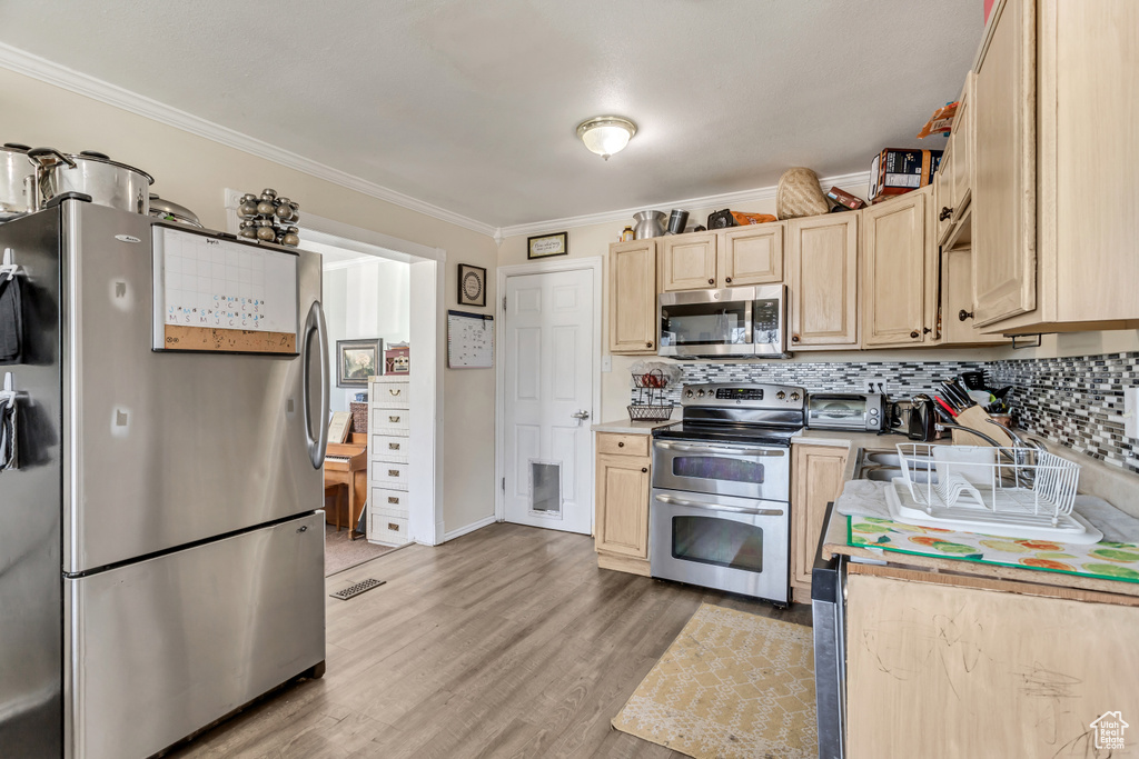 Kitchen featuring crown molding, light hardwood / wood-style flooring, light brown cabinets, backsplash, and appliances with stainless steel finishes