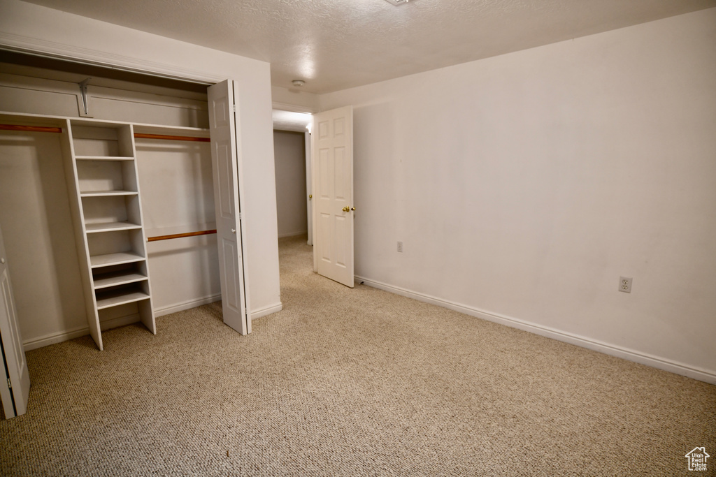 Unfurnished bedroom with light colored carpet, a closet, and a textured ceiling