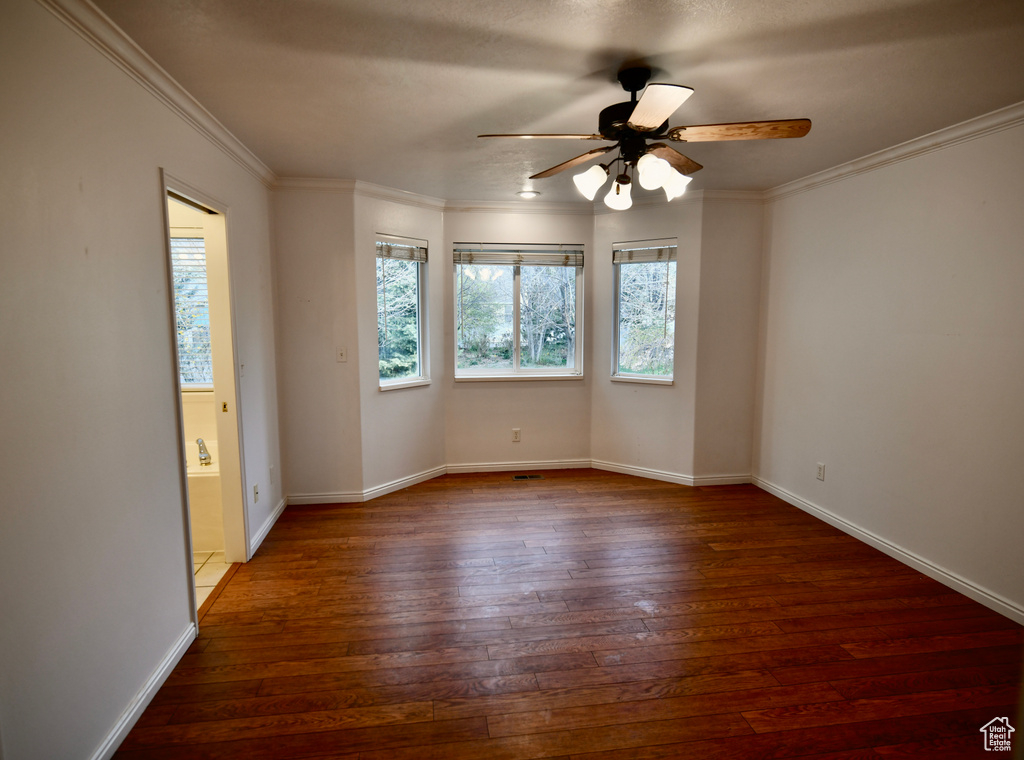 Empty room featuring dark hardwood / wood-style flooring, ceiling fan, and crown molding