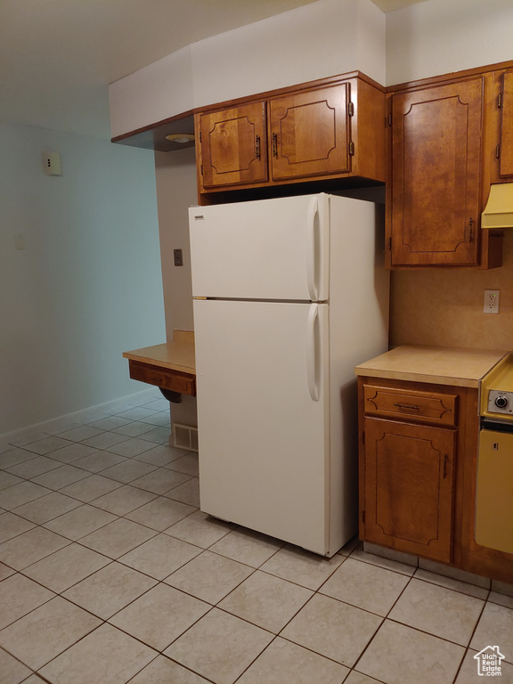 Kitchen with light tile flooring, premium range hood, and white refrigerator