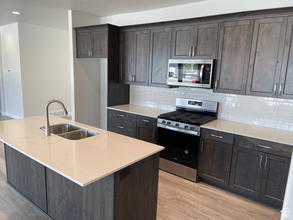 Kitchen featuring appliances with stainless steel finishes, light hardwood / wood-style flooring, sink, and a center island with sink