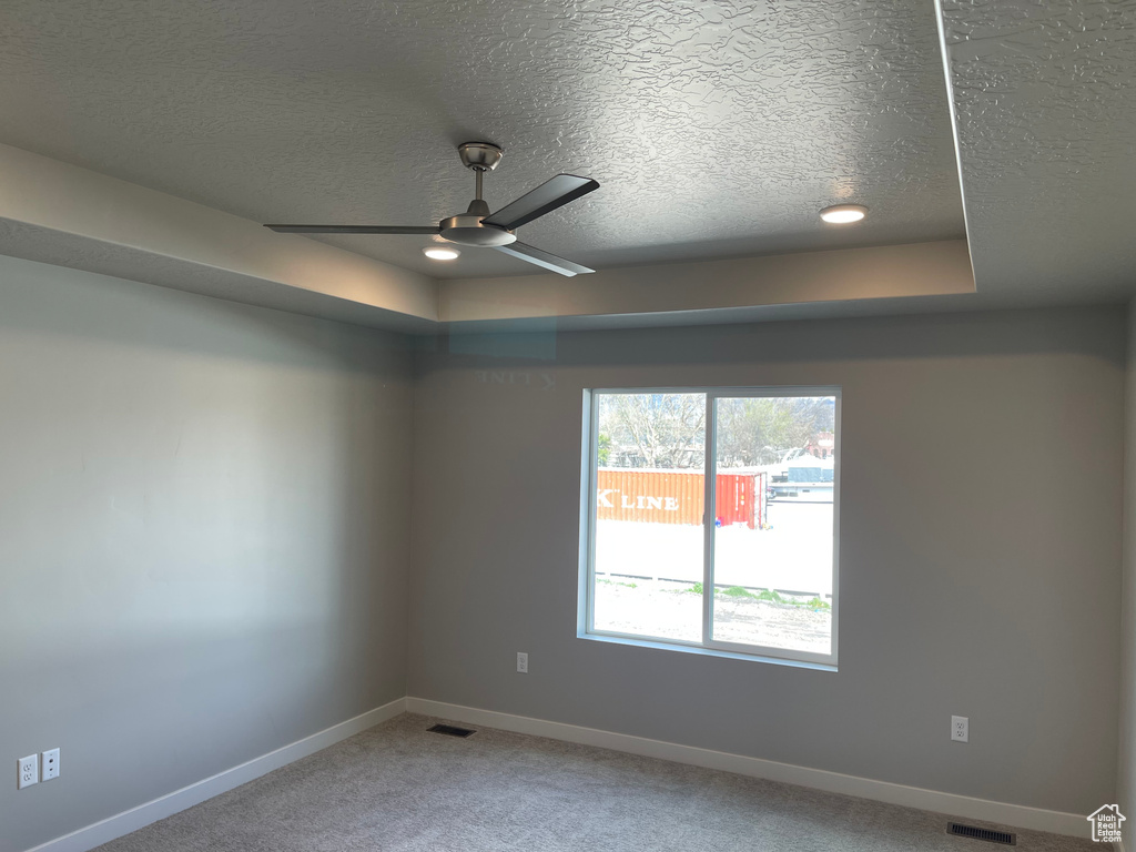 Spare room featuring light colored carpet, a textured ceiling, ceiling fan, and a tray ceiling