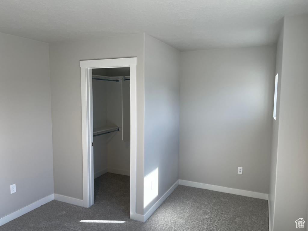 Unfurnished bedroom featuring a spacious closet, a closet, and dark colored carpet