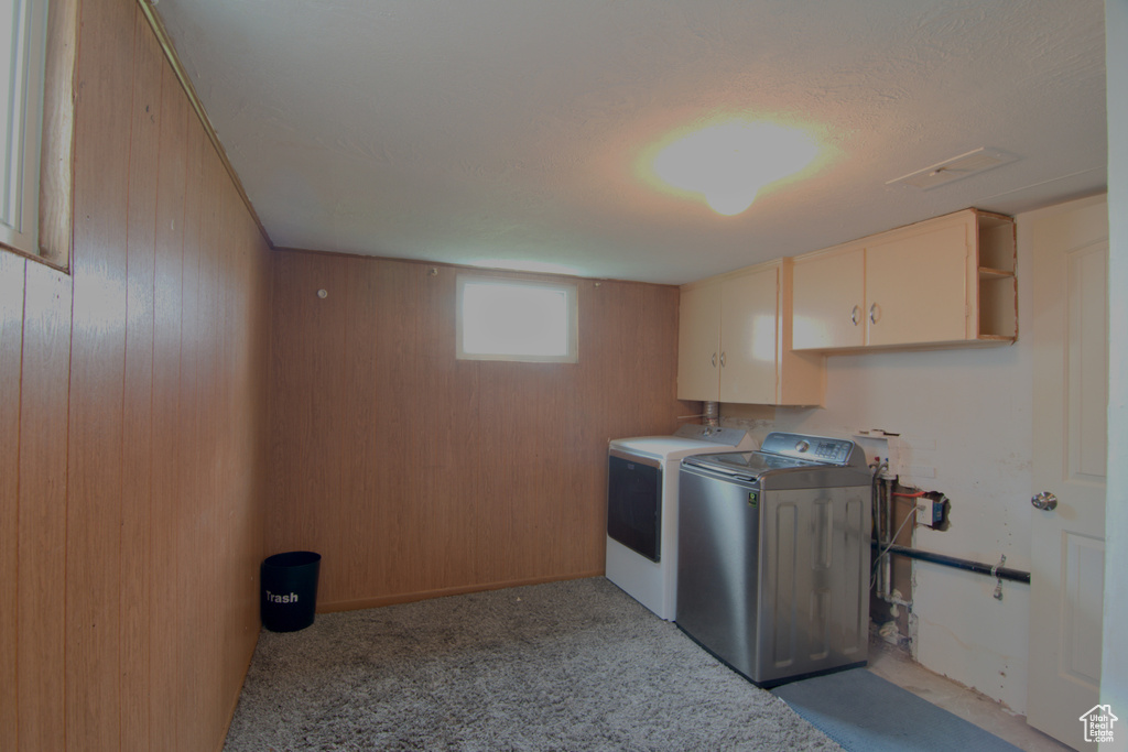 Laundry area featuring light colored carpet, cabinets, washer and dryer, and wooden walls